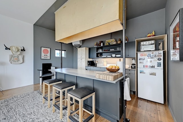 kitchen featuring a breakfast bar, freestanding refrigerator, light countertops, light wood-style floors, and open shelves