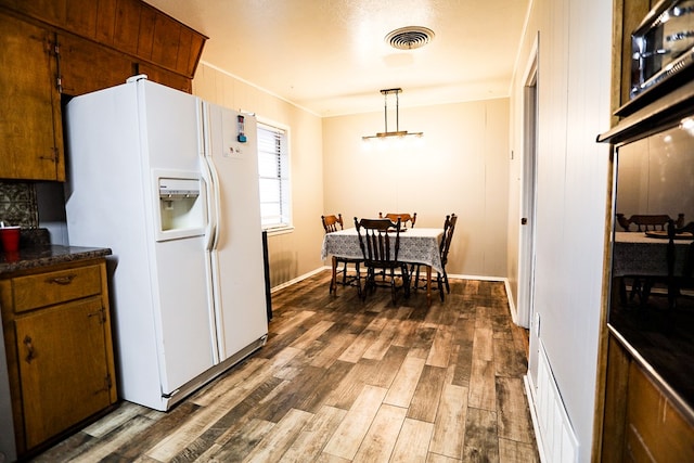 kitchen featuring visible vents, dark wood finished floors, white refrigerator with ice dispenser, dark countertops, and brown cabinets