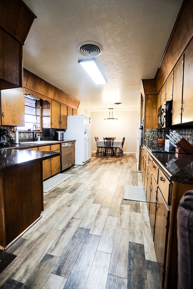 kitchen featuring dark countertops, visible vents, white refrigerator with ice dispenser, and stainless steel dishwasher