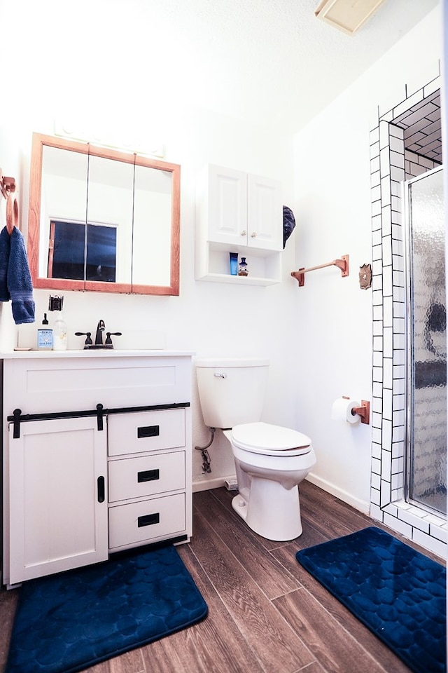 full bath with a shower stall, baseboards, toilet, wood finished floors, and vanity