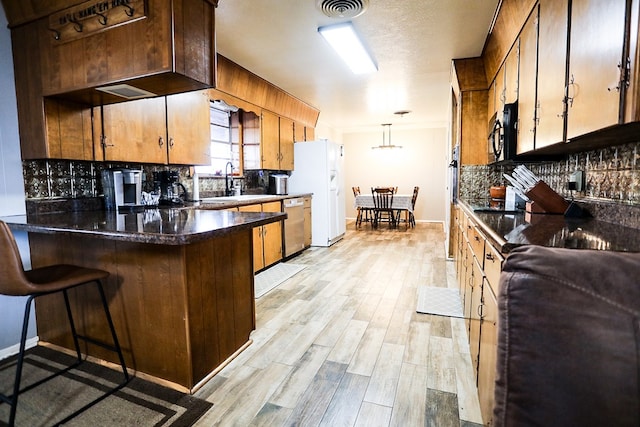 kitchen with visible vents, light wood-style flooring, backsplash, a peninsula, and dishwasher