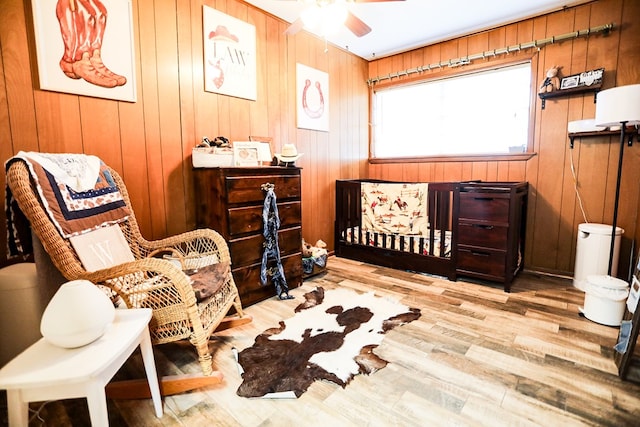 sitting room featuring wood finished floors, wooden walls, and a ceiling fan