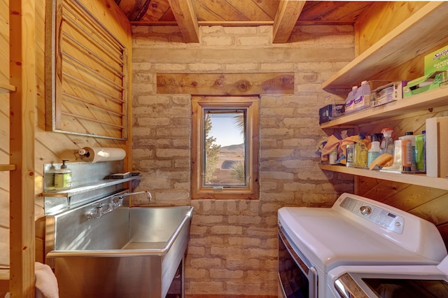 clothes washing area with washer and clothes dryer and brick wall