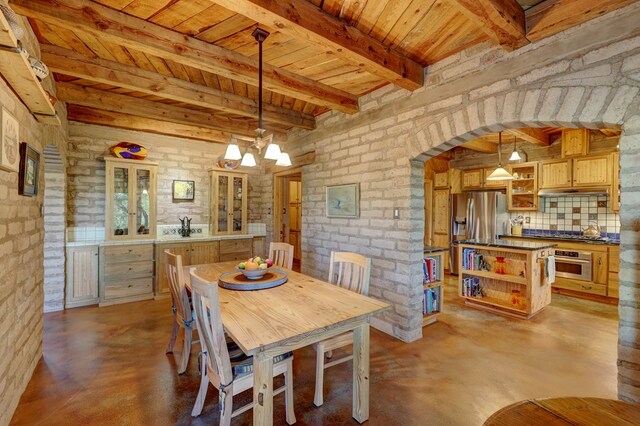 dining space with beamed ceiling, an inviting chandelier, wood ceiling, and brick wall