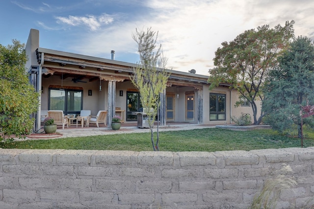 rear view of house featuring ceiling fan, a patio area, and a lawn