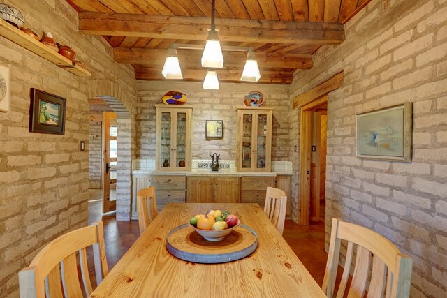 dining area featuring beamed ceiling, wood ceiling, and brick wall