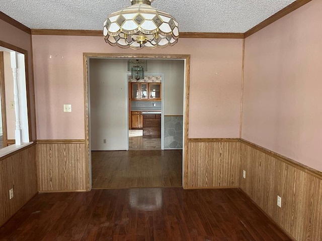 unfurnished dining area featuring wooden walls, wainscoting, a textured ceiling, and wood finished floors