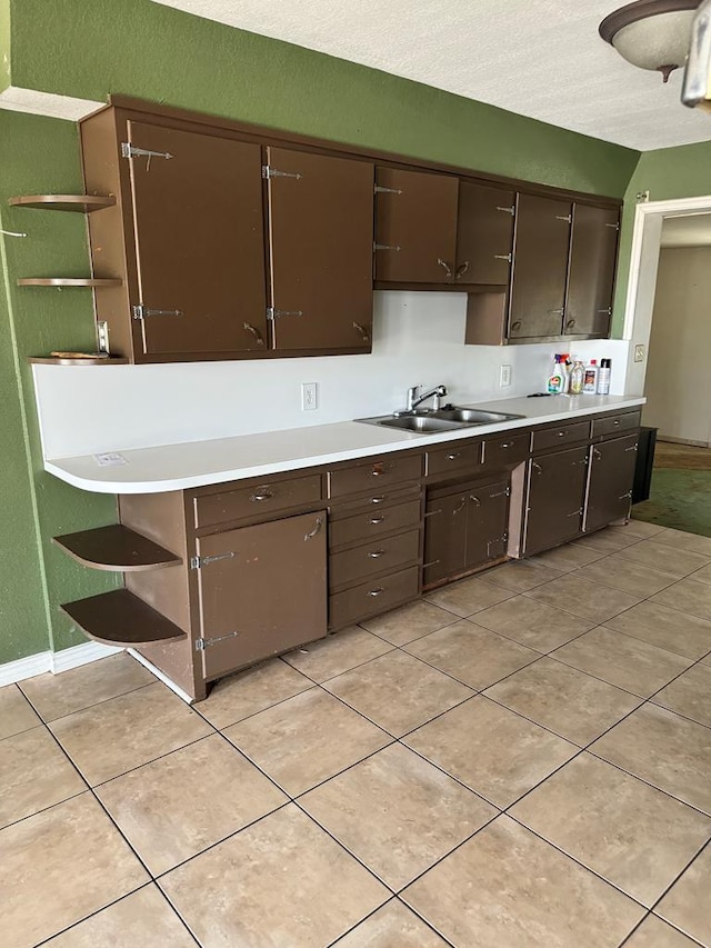 kitchen with dark brown cabinetry, sink, and light tile patterned floors