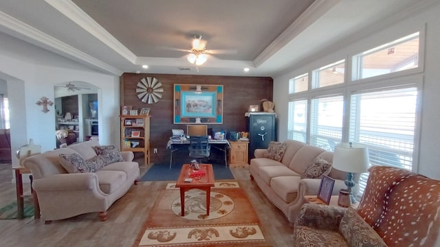 living room featuring a raised ceiling, light wood-type flooring, and crown molding