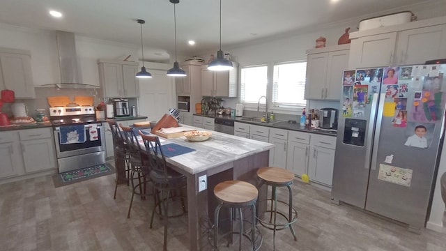 kitchen with wall chimney range hood, sink, light wood-type flooring, appliances with stainless steel finishes, and decorative light fixtures