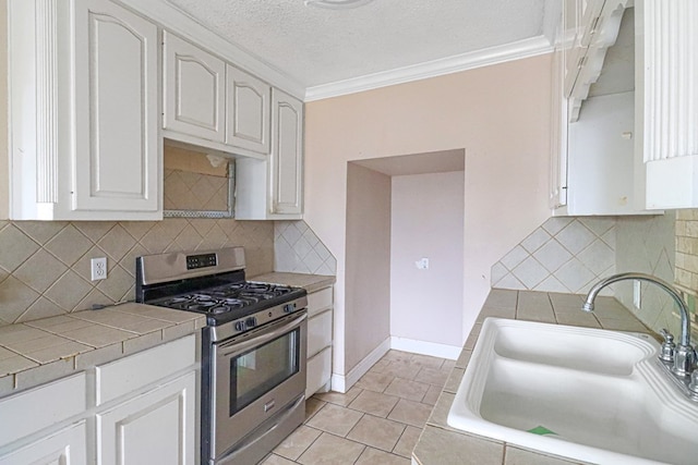 kitchen with decorative backsplash, white cabinets, sink, stainless steel gas range oven, and tile countertops