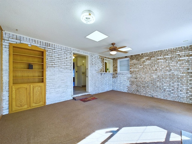 empty room featuring a textured ceiling, ceiling fan, brick wall, and carpet floors