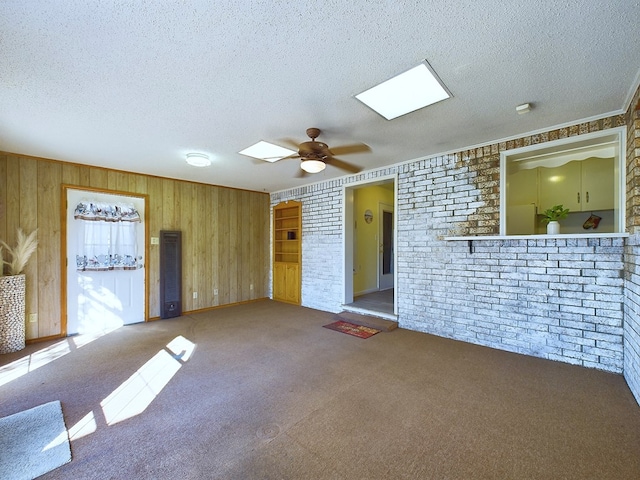 carpeted empty room with ceiling fan, wooden walls, a textured ceiling, and ornamental molding