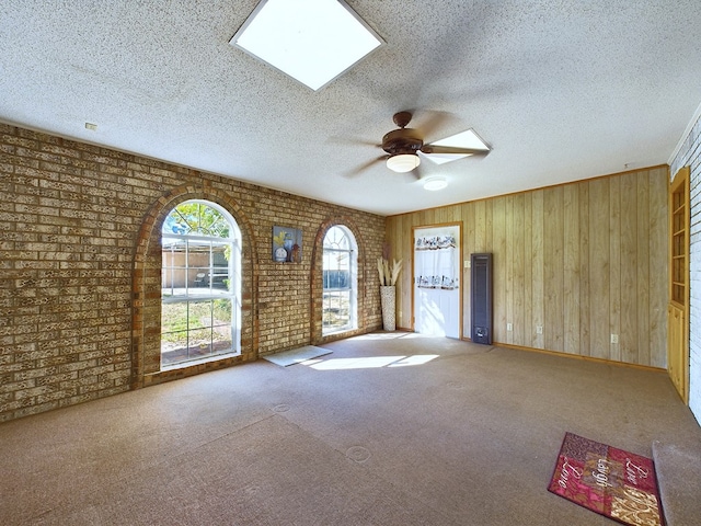 carpeted empty room featuring ceiling fan, a textured ceiling, brick wall, and wooden walls