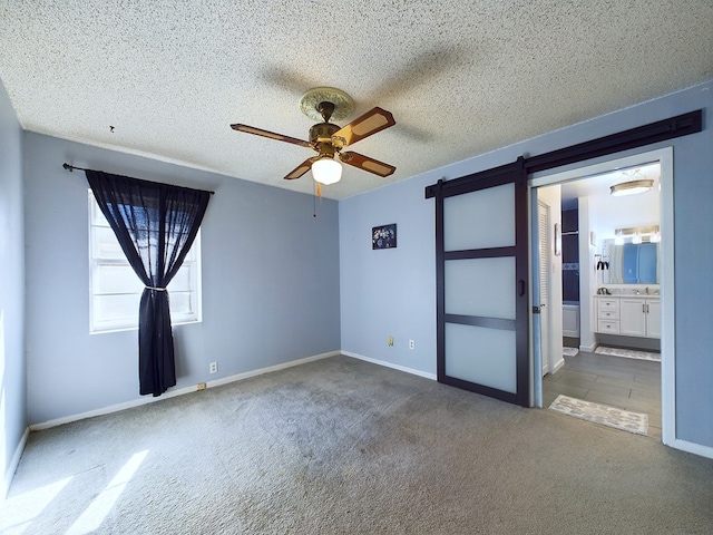 carpeted spare room featuring ceiling fan, a barn door, and a textured ceiling