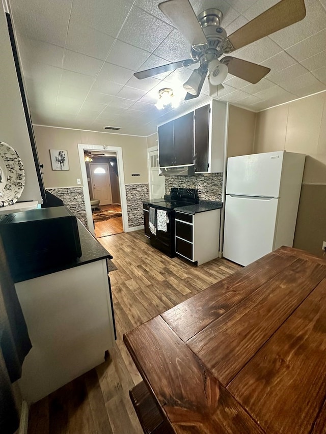 kitchen featuring backsplash, light hardwood / wood-style floors, white refrigerator, ceiling fan, and black / electric stove