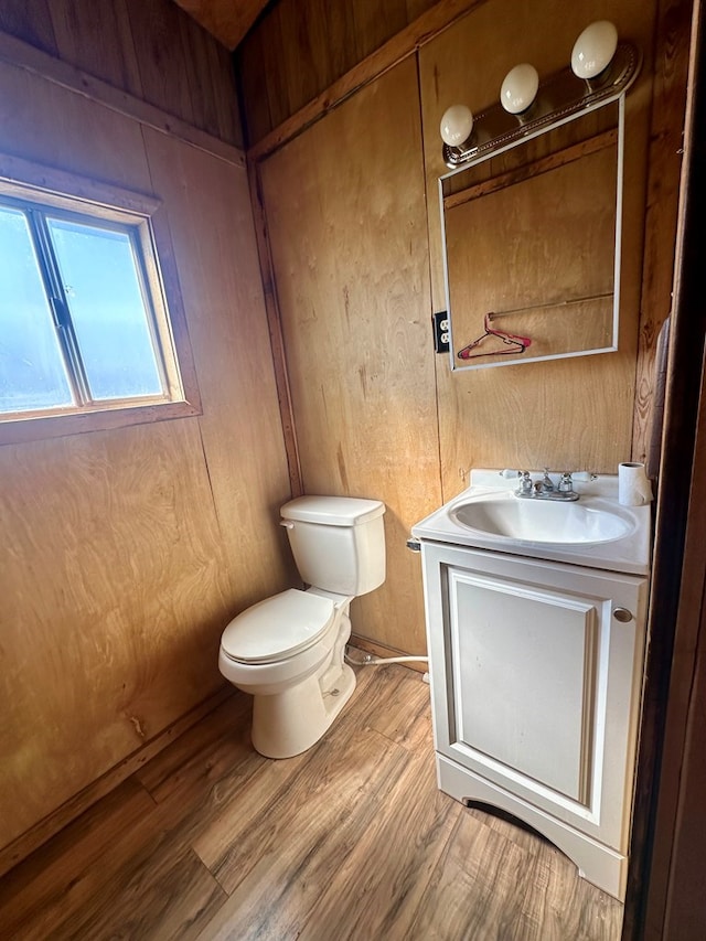 bathroom with toilet, wood-type flooring, wood walls, and vanity