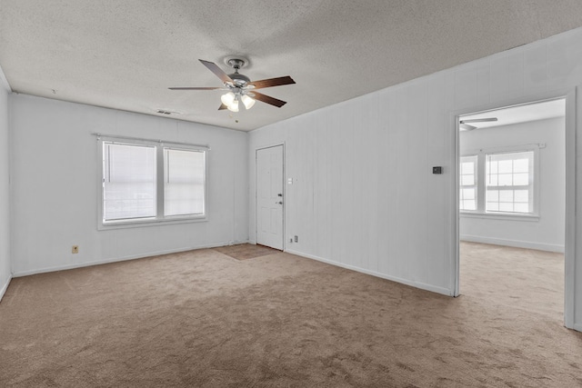 carpeted empty room featuring a textured ceiling, ornamental molding, a ceiling fan, and baseboards