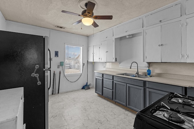 kitchen with black gas range oven, freestanding refrigerator, gray cabinets, a textured ceiling, and a sink