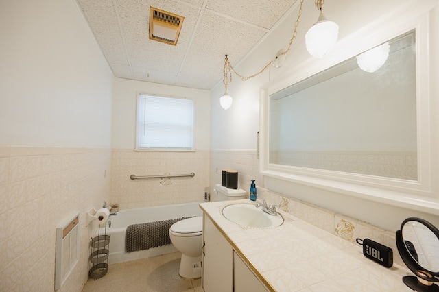 bathroom featuring a paneled ceiling, vanity, tile walls, and a tub