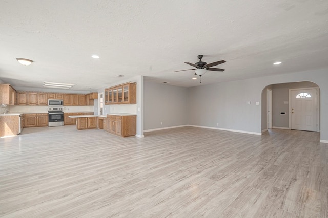 unfurnished living room featuring light wood finished floors, arched walkways, a textured ceiling, and baseboards