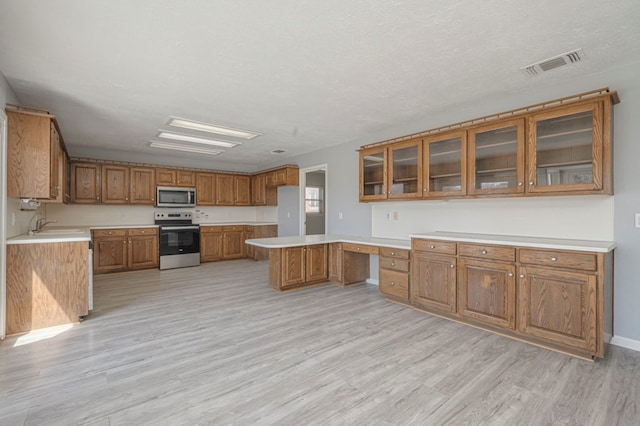 kitchen with visible vents, brown cabinets, stainless steel appliances, light wood finished floors, and built in study area