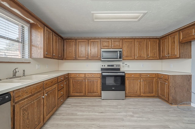 kitchen with brown cabinetry, light wood-style flooring, a sink, stainless steel appliances, and a textured ceiling