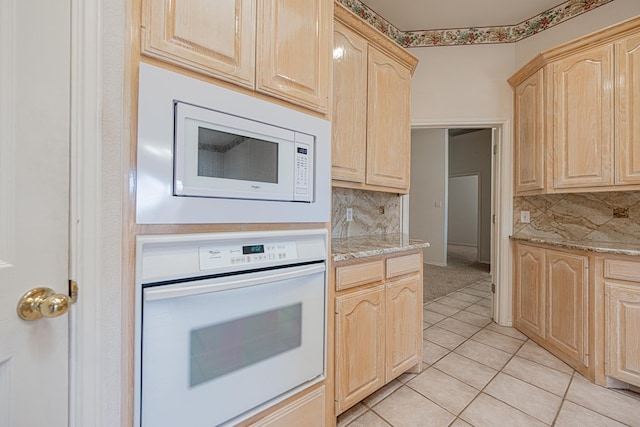 kitchen featuring light stone counters, white appliances, light brown cabinetry, and backsplash