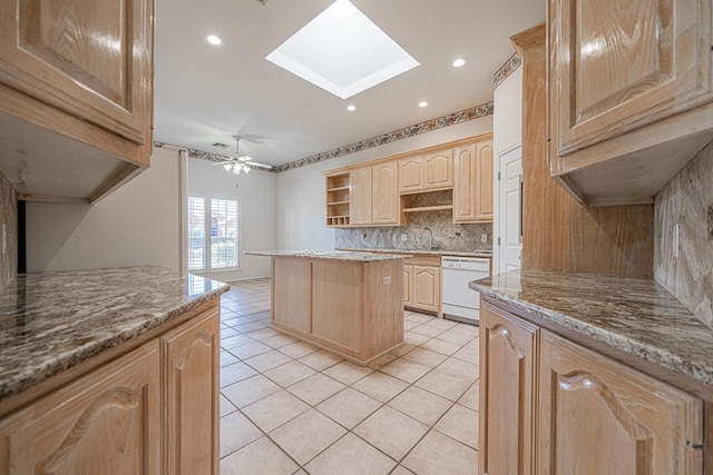 kitchen with a skylight, white dishwasher, light stone counters, a kitchen island, and light brown cabinetry