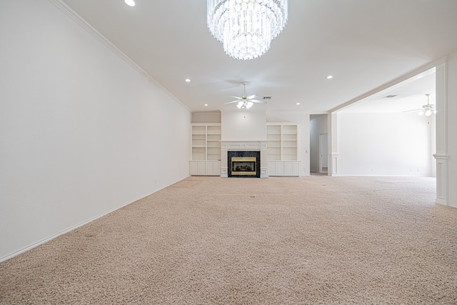 unfurnished living room featuring built in shelves, ornamental molding, light colored carpet, a fireplace, and ceiling fan with notable chandelier