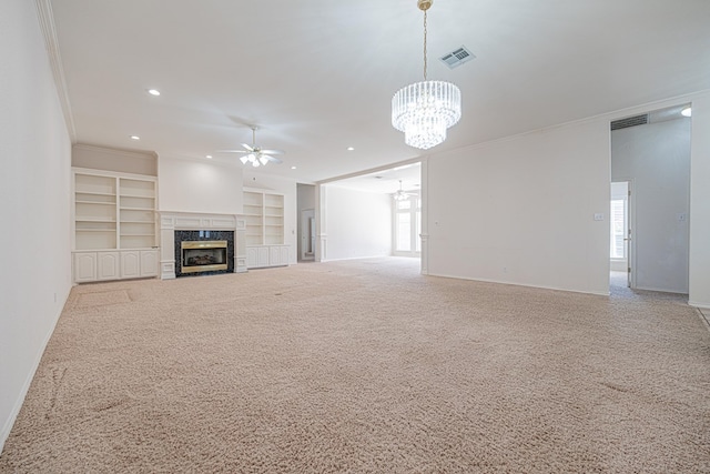 unfurnished living room with built in features, a high end fireplace, ornamental molding, ceiling fan with notable chandelier, and light colored carpet