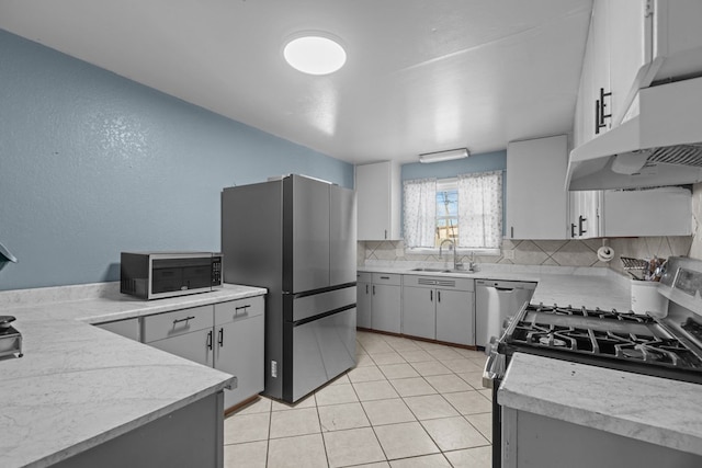 kitchen with gray cabinetry, a sink, under cabinet range hood, appliances with stainless steel finishes, and tasteful backsplash