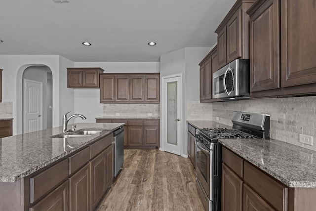 kitchen with appliances with stainless steel finishes, a sink, a center island with sink, and wood finished floors