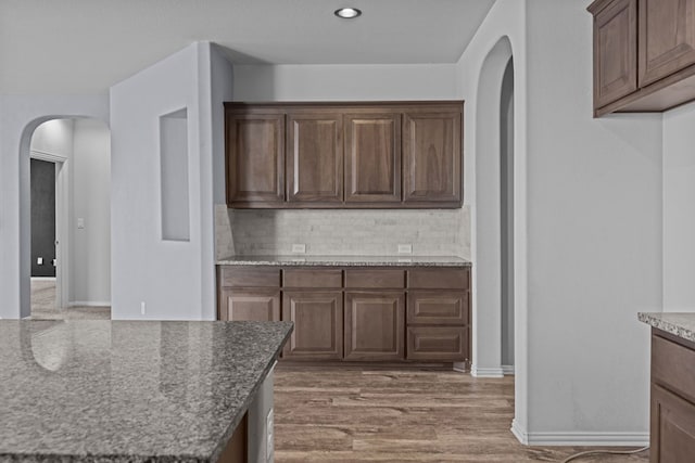 kitchen with tasteful backsplash, arched walkways, baseboards, wood finished floors, and stone counters