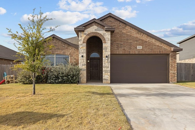 french country inspired facade with a garage, a front yard, concrete driveway, and brick siding