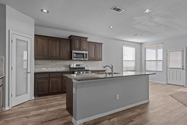 kitchen with dark brown cabinetry, an island with sink, wood finished floors, stainless steel appliances, and a sink