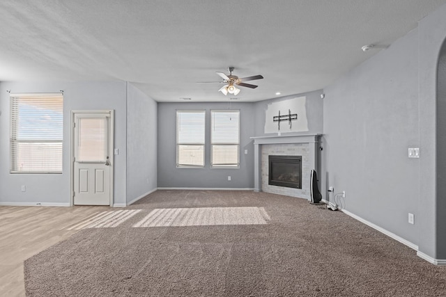 unfurnished living room with ceiling fan, baseboards, a textured ceiling, and a glass covered fireplace