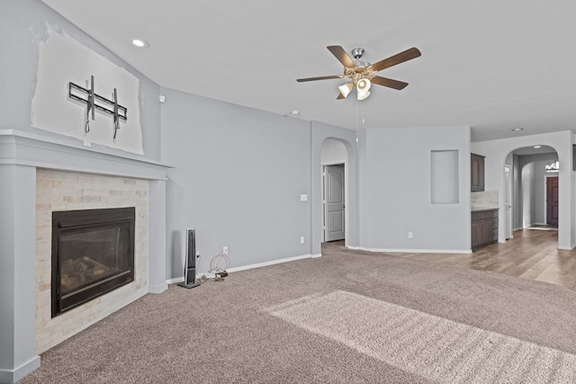 unfurnished living room featuring arched walkways, a glass covered fireplace, carpet flooring, and baseboards