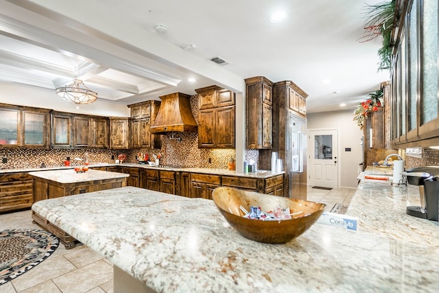 kitchen featuring stainless steel gas cooktop, beamed ceiling, premium range hood, backsplash, and a kitchen island