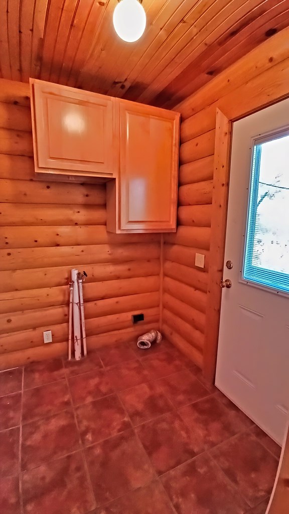 laundry area featuring rustic walls, cabinets, and wooden ceiling