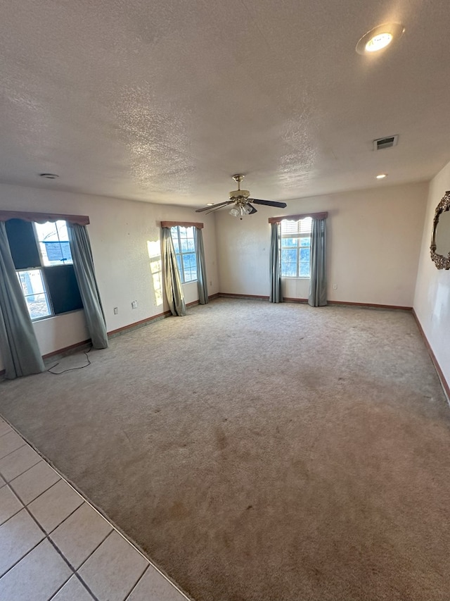 empty room with ceiling fan, a textured ceiling, a healthy amount of sunlight, and carpet flooring