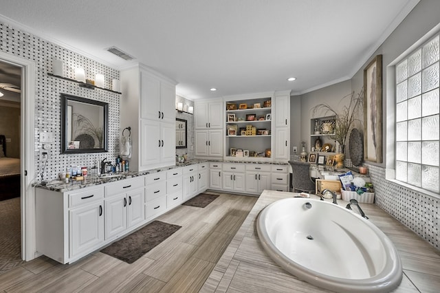 full bathroom featuring a garden tub, double vanity, visible vents, ornamental molding, and a sink