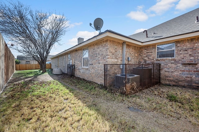 view of side of property featuring brick siding, a chimney, a lawn, central AC unit, and fence