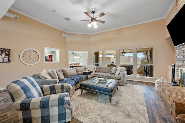 living room with a fireplace, ornamental molding, dark wood-type flooring, and ceiling fan with notable chandelier