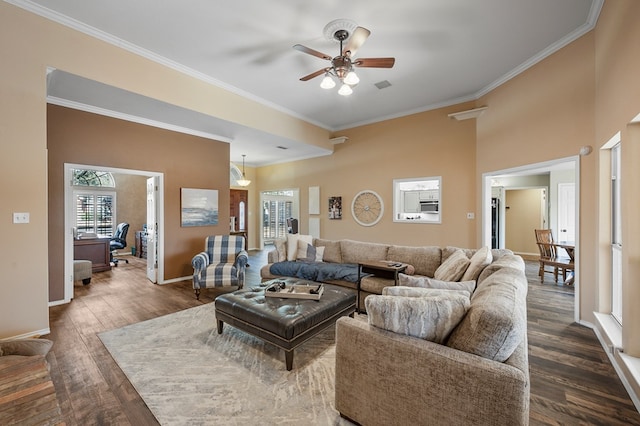 living area featuring dark wood-style flooring, a ceiling fan, visible vents, baseboards, and ornamental molding