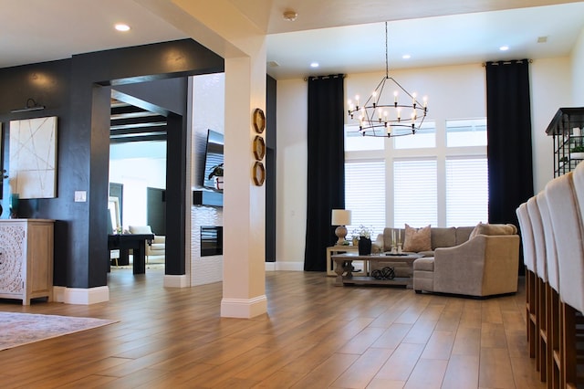 living area featuring a chandelier, recessed lighting, baseboards, light wood-style floors, and a glass covered fireplace