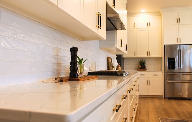 kitchen with range hood, light wood finished floors, decorative backsplash, white cabinets, and stainless steel fridge