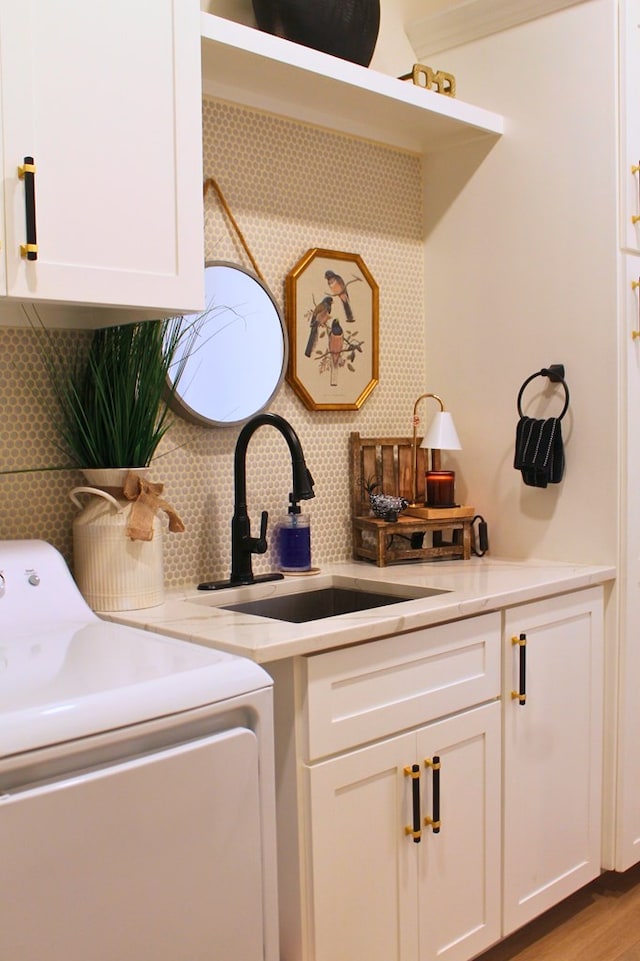 clothes washing area featuring light wood-style floors, cabinet space, and a sink