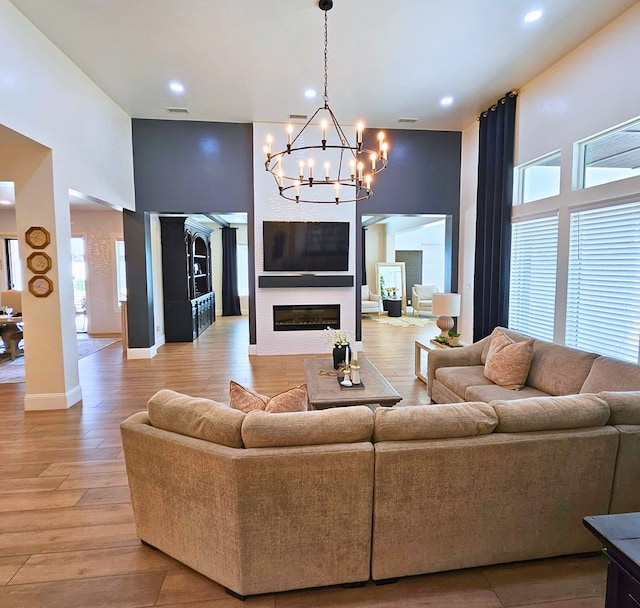 living room with a towering ceiling, light wood finished floors, baseboards, and a glass covered fireplace