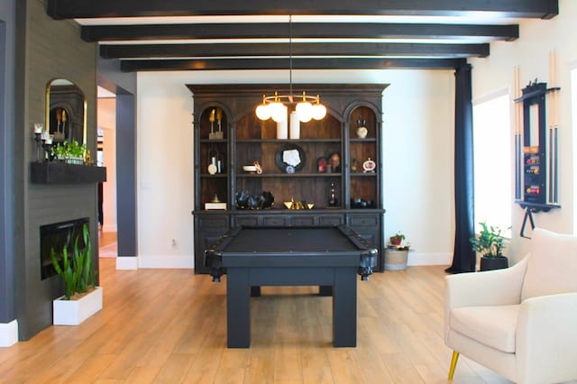 game room featuring light wood-type flooring, beam ceiling, a glass covered fireplace, and baseboards